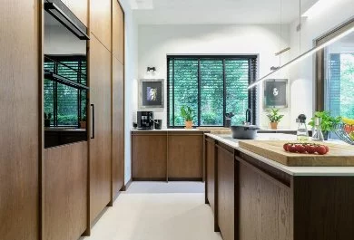 Przestronna kuchnia w kolorze ciemnego drewna, z jasnymi blatami i czarnymi sprzętami AGD