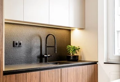 Detal kuchni z drewnianymi frontami, czarnym blatem i matową czarną baterią.