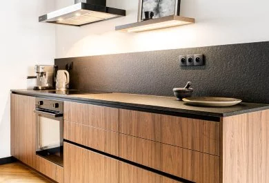 Strefa gotowania z piekarnikiem, czarnym okapem i drewnianą zabudową dolną.