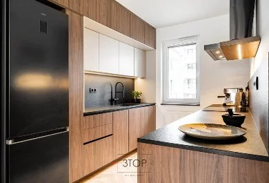 Nowoczesna kuchnia z drewnianymi frontami, czarną lodówką i półwyspem z ciemnym blatem.