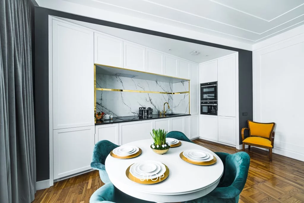 Otwarta, biało-szara kuchnia narożna ze złotą armaturą